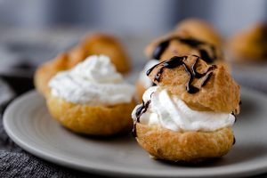 Cream puffs with whipped cream and a chocolate drizzle over the top.