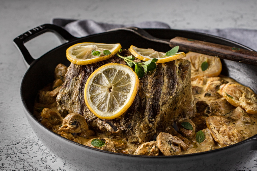Pot Roast in Sour Cream with mushrooms and lemons in a grey Dutch oven with a serving fork laying across the pan.