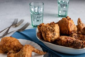 Several pieces of fried chicken stacking in a bowl and two pieces on a plate.